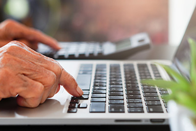 Senior Hands Typing on a Laptop and a Calculator