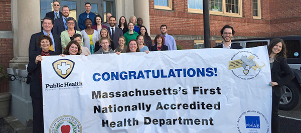 People Holding Massachusetts's First Nationally Accredited Health Department Banner Outside of Building
