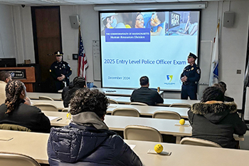 Group Sitting at Desks Watching Presentation on Entry Level Police Officer Exam on Projection Screen