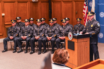 Swearing In Ceremony at City Hall with Police Officials Sitting in Charis and Police Chief at Podium