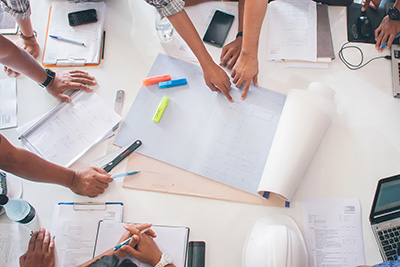 Group of People Sitting Around Conference Table with Blueprints and Building Plans Being Reviewed