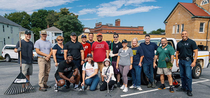 Group Photo of Members of Quality of Life Team Standing in Parking Lot Holding Rakes and Yard Tools