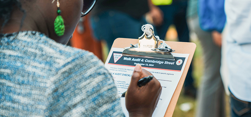 Looking Over Woman's Shoulder Holding Clipboard with Walk Audit Checklist for Cambridge Street