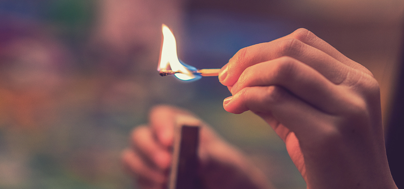 Hand Holding Lit Match and Box of Matches