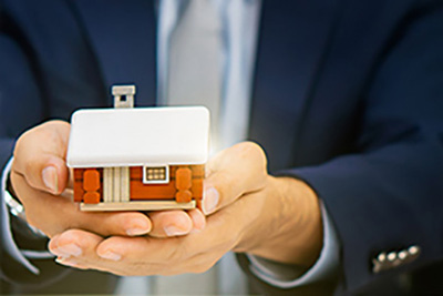 Business Man Holding a Wooden House in His Hands