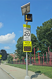 School Speed Limit Sign with Flashing Speed Indicator Beacon on Pole Near School Playground