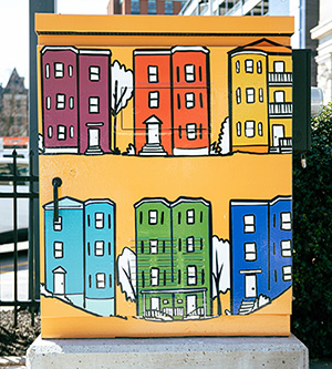 WooBox painted yellow with drawings of multi-colored triple decker buildings