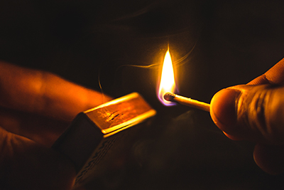 Hands Striking Match on Matchbox in the Dark