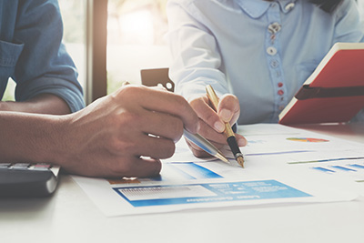 Two People Looking at Plans Printed Out on Table with Other Paperwork Around